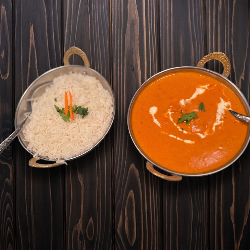 Orange curry with cream swirl and white rice, served in metal bowls on a dark wooden surface.