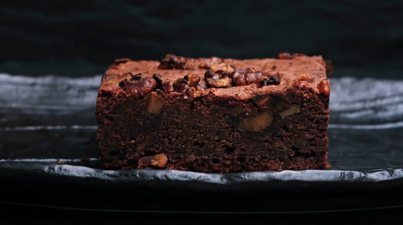 Rich chocolate brownie with walnuts and chocolate chunks on a dark plate.